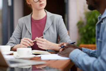Close-up of African man and young businesswoman sitting at the table working with documents and discussing some project together in cafe
