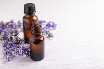 Bottles of essential oil and lavender flowers on white wooden background. Space for text