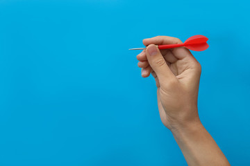 Woman holding red dart on blue background, closeup. Space for text