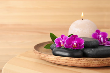 Tray with spa stones, orchid flowers and candle on wooden table. Space for text