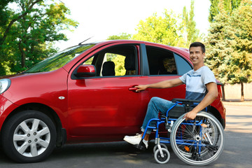 Young man in wheelchair opening door of car outdoors