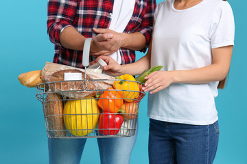 Young couple with shopping basket full of products on blue background, closeup