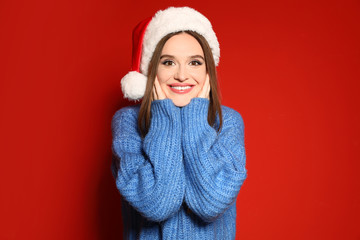 Young woman in Christmas sweater and Santa hat on red background