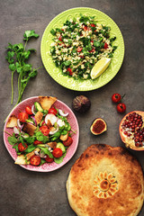 Middle Eastern salads tabbouleh and fattoush, pitta bread, pomegranate, figs on a dark rustic background. Arabic dishes, top view.