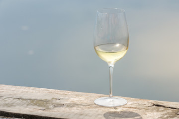 Still life of the glass of white wine on the edge of lake with reflection of the sky. Copy space background for alcohol consumption concept.
