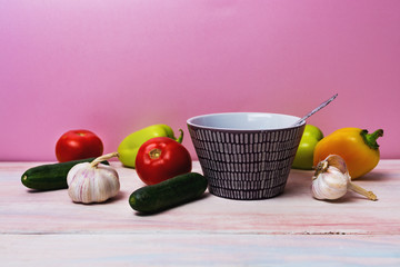 bell pepper, garlic, bowl, cucumbers and tomatoes on pink background