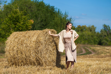 Naklejka na ściany i meble Beautiful girl in a beige suit posing on a background of haystacks in a cut field