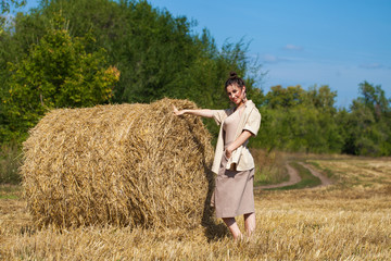 Beautiful girl in a beige suit posing on a background of haystacks in a cut field