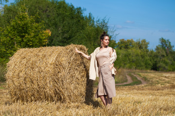 Beautiful girl in a beige suit posing on a background of haystacks in a cut field