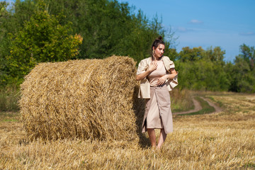 Naklejka na ściany i meble Beautiful girl in a beige suit posing on a background of haystacks in a cut field