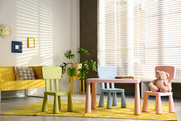 Stylish playroom interior with table, chairs and sofa