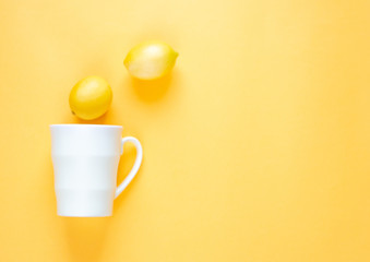 Mug and two lemons on a yellow background. There is a place for text. Tea with lemon.