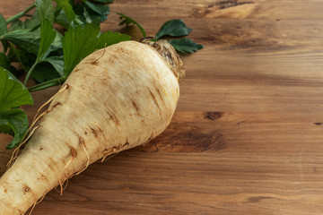  Parsnip root with green leaves lies on a brown wooden surface on the left, on the right is an empty place, top view