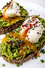 Poached eggs with avocado guacomole on brown bread with sesame seeds. Healthy breakfast on a white background.