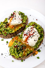 Poached eggs with avocado guacomole on brown bread with sesame seeds. Healthy breakfast on a white background.