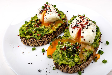 Poached eggs with avocado guacomole on brown bread with sesame seeds. Healthy breakfast on a white background.