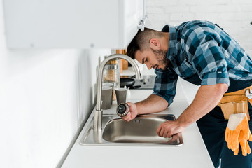 selective focus of handsome bearded repairman working near sink in kitchen