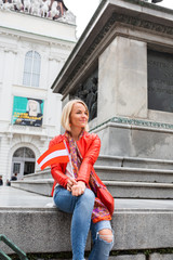 Young woman sits on a monument in front of the Austrian National Library with the flag of Austria in her hands, Vienna