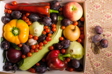 Rural still life. Vegetables and fruits in a white box. Tablecloth of autumn colors with plums and dry leaf.