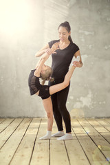 Graceful little girl ballerina standing on hands and stretching with teacher in dance studio