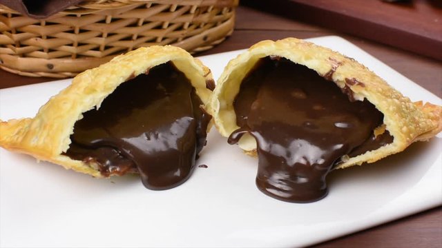 One open traditional Brazilian fried pastry called pastel stuffed with chocolate Brazilian dessert brigadeiro in plate a in wood background