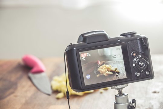 Camera shooting a photo of chopped potatoes on a wooden surface with a knife on the side