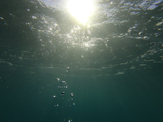 Underwater bubbles with sunlight through water surface as seen in natural scene at Caribbean turquoise open ocean sea