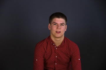 Portrait of a guy of European appearance in a red shirt, the guy's face is covered with acne.  Shooting in the studio, plain background.