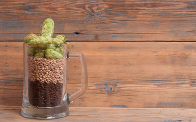 Glass mug of grain and hops on a old wooden table.