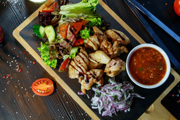 Pork kebab with tomato sauce and greens on a cutting board on a black wooden background