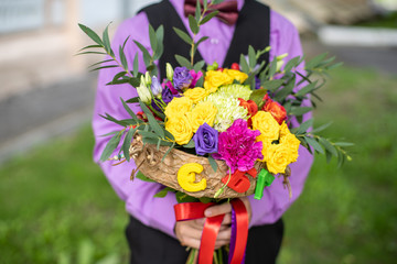 Boy in purple shirt bow tie holding a festive bright pink and yellow bouquet of flowers on first of September