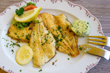 fried plaice fillet with herb butter and lemon on a plate, typical food in northern germany at the...