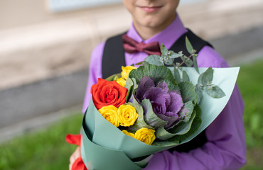 Boy in purple shirt with bow tie holding a festive bright pink and yellow bouquet of flowers on first of September