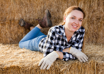 Naklejka na ściany i meble Young female farmer worker resting on hay during break