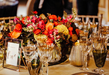 Table set for an event party or wedding reception. Beautiful flowers and glassware set on the table. Selective focus on flowers. Warm colours.