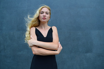 Young blonde girl folded her arms in black dress against grey background.