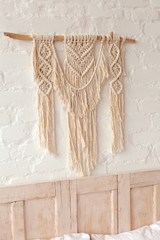 Big macrame in neutral tones on a white brick wall in Scandinavian style bedroom