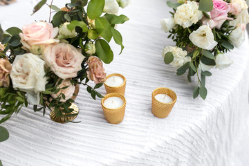 Wedding table setting decorated with fresh flowers in a brass vase. Wedding floristry. Banquet table for guests outdoors with a view of green nature. Bouquet with roses, eustoma and eucalyptus leaves