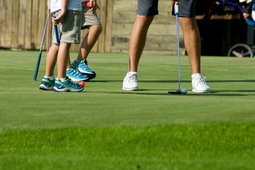 young boy giving a lesson on a golf course green to pull ball into hole, grass, sunset, teacher, sports, concentration, hobby, child, mountain, vacation, Trentino, Alto Adige, Italy