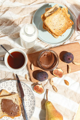 Appetizing toasts with chocolate paste, tea, figs, blueberries and almonds on the table.