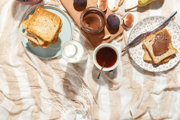 Appetizing toasts with chocolate paste, tea, figs, blueberries and almonds on the table.