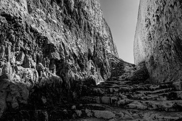 Monochrome photography, hazardous direction and explore seduced pathway conceptual idea with horizontal black and white photograph of dangerous path between steep chalk peaks and rugged terrain