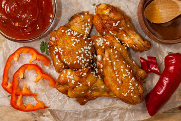 Fried juicy chicken wings marinated with honey, soy sauce, spices, sprinkled with sesame seeds on paper on a wooden background. Asian recipe, top view, close up