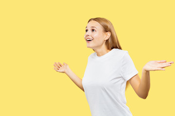 Caucasian young woman's half-length portrait on yellow studio background. Beautiful female model in white shirt. Concept of human emotions, facial expression. Showing an empty bar and smiling.