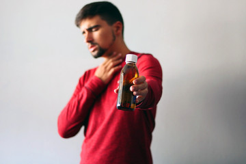 Health and Medicine Concept: Young boy cold dressed in red holding a cough syrup.