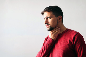 Medicine and Health Concept: Young boy dressed in red with a sore throat on a white background.