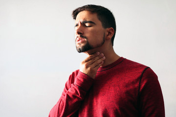 Medicine and Health Concept: Young boy dressed in red with a sore throat on a white background.