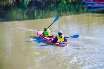 Father and son in kayak boat on pond with father watching boy row from behind - reflections and moored boats in background - the Gathering Place public park in Tulsa USA