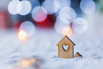 Wooden icon of house with hole in form of heart with red home Christmas decor and blurred bokeh...