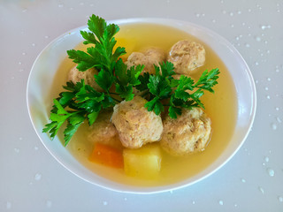 Meatballs and potatoes in vegetable soup in a white plate.